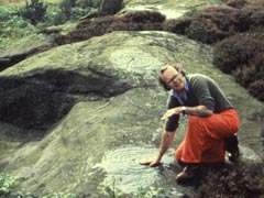 Stan Beckensall crouching beside cup and ring marked rocks